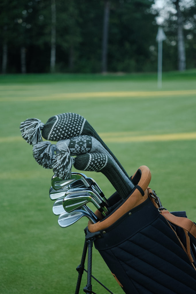 Green knit wool golf headcovers with Nordic patterns in a carry bag next to the green – classic and premium golf accessories for players with refined taste.